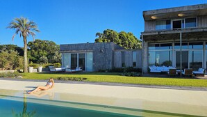 A modern house with a swimming pool, outdoor seating, and a stone wall. - Luxury 10,000 sq ft modern house with breathtaking ocean views and every amenity (José Ignacio)