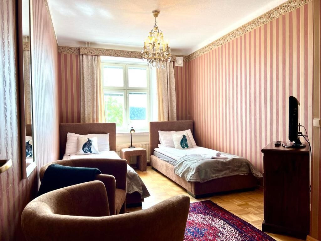 Une chambre avec deux lits, un lustre, un bureau et une fenêtre avec des rideaux.