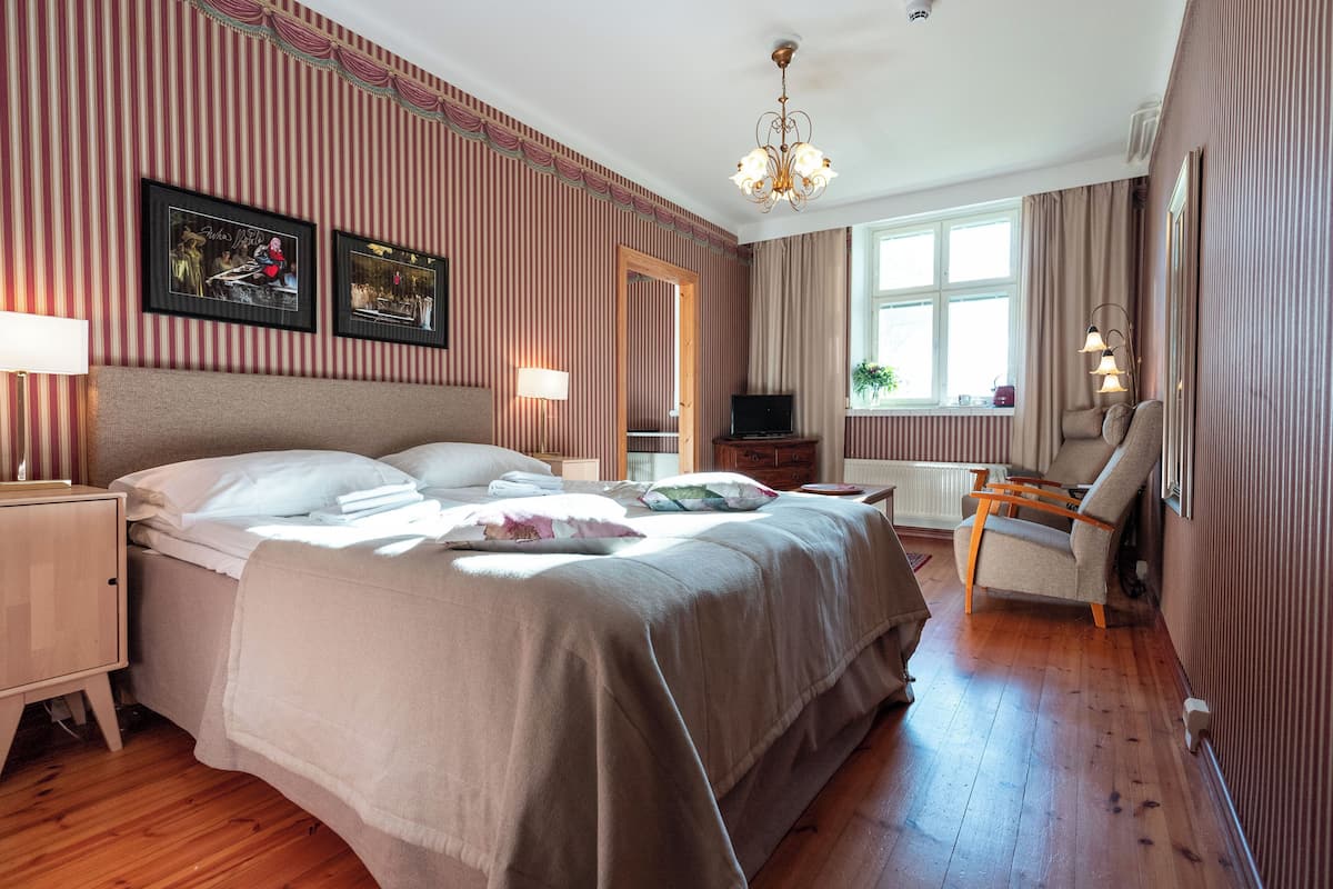 Ein Hotelzimmer mit einem großen Bett, einem Fernseher, einem Sessel und einem Fenster mit Vorhängen.