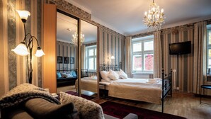 Een hotelkamer met een groot bed, een zithoek met een bank, een televisie en een kroonluchter.