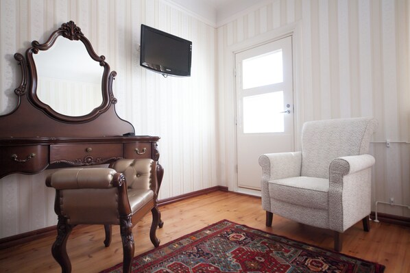 A room with a wooden dresser, a mirror, a television, a patterned armchair, and a patterned rug. - Hotel Hospitz (Savonlinna)