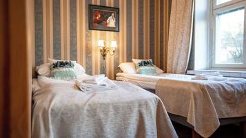 Ein Hotelzimmer mit zwei Einzelbetten, einem gerahmten Bild an der Wand und einem Fenster mit Vorhängen.