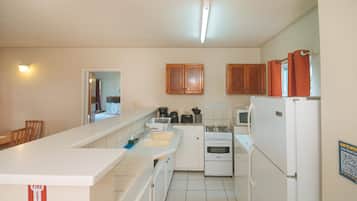 Una cocina compacta con armarios blancos, estufa, horno y refrigerador. Hay un fregadero y una encimera con varios utensilios de cocina.