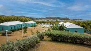 A coastal property with two turquoise buildings, a swimming pool, and a view of the sea and hills. - Neem View Apartments Antigua (Falmouth Harbour)