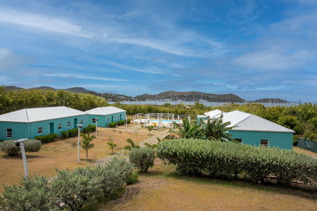 A coastal property with two turquoise buildings, a swimming pool, and a view of the sea and hills.
