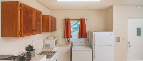 A compact kitchen with wooden cabinets, a microwave, a stove, a washing machine, and a refrigerator.