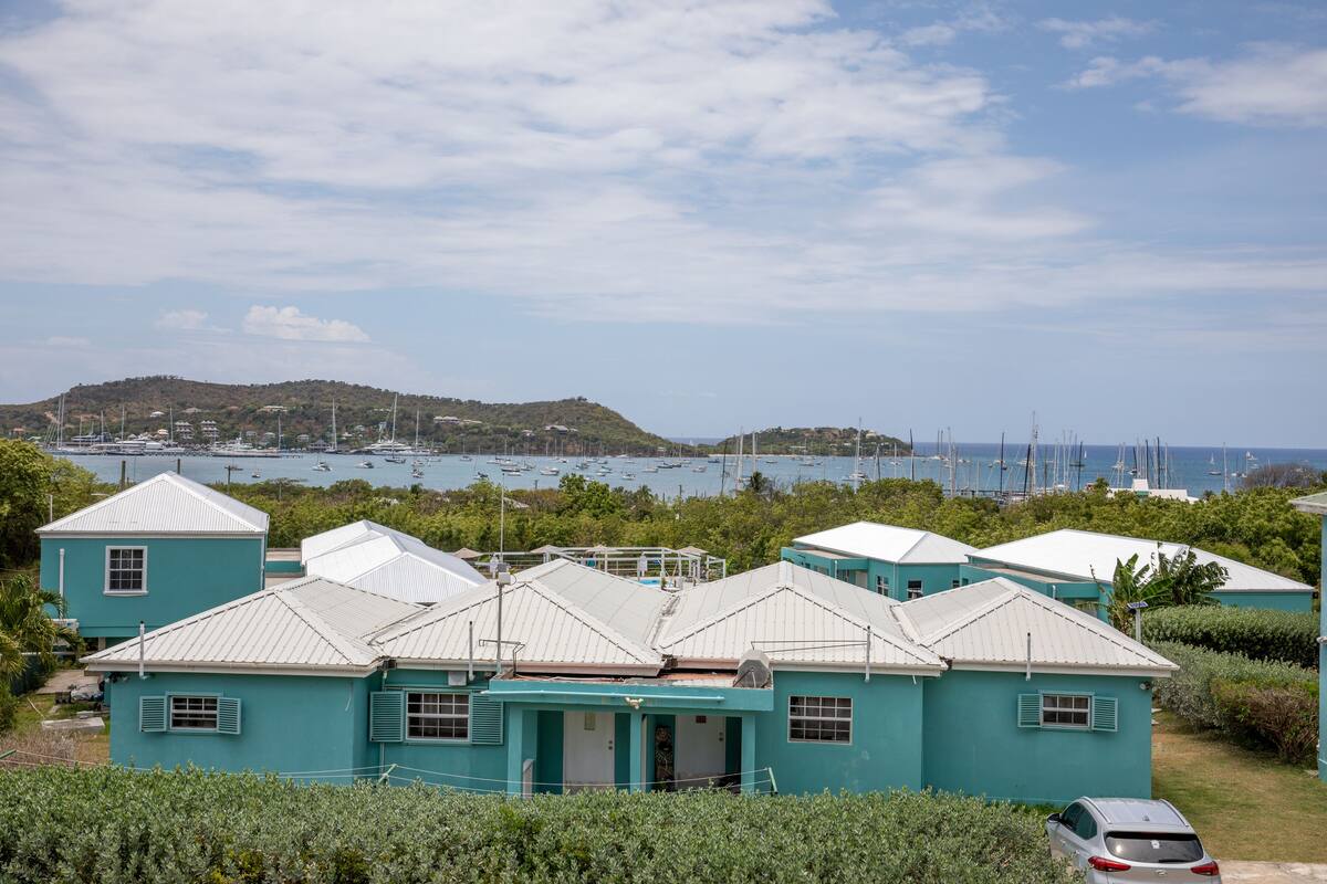 A coastal area with turquoise buildings, a marina with boats, and a hilly landscape in the background.