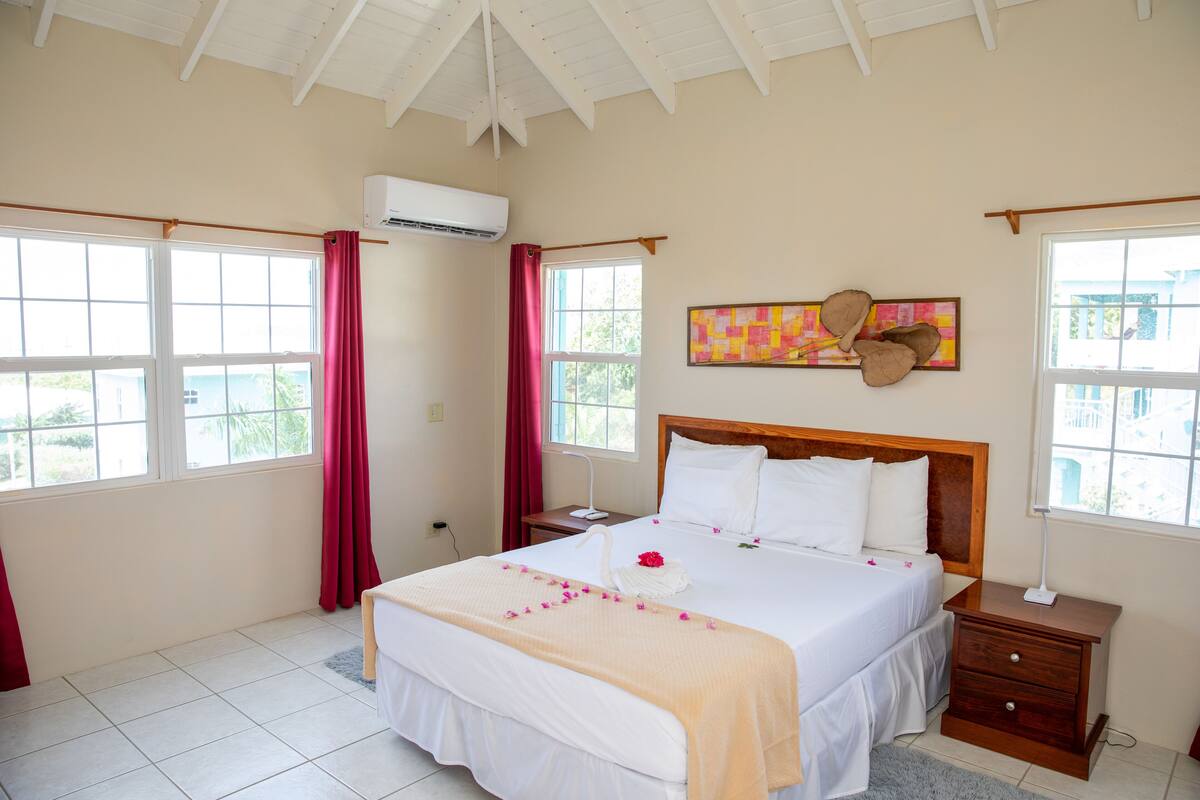 A hotel room with a large bed, a wooden headboard, a bedside table, a nightstand, and a window with curtains.