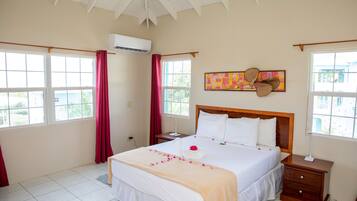 A hotel room with a large bed, a wooden headboard, a bedside table, a nightstand, and a window with curtains.