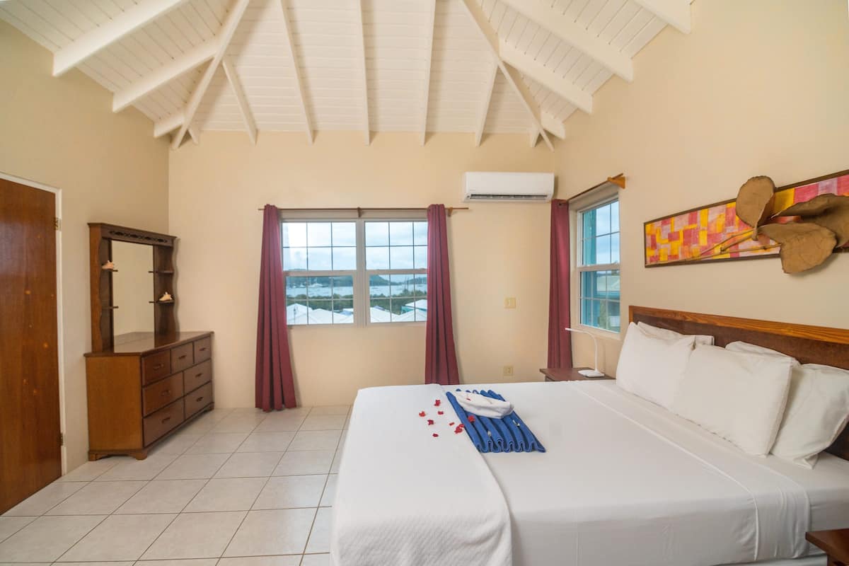 A hotel room with a large bed, a wooden dresser, a mirror, and a window with curtains.