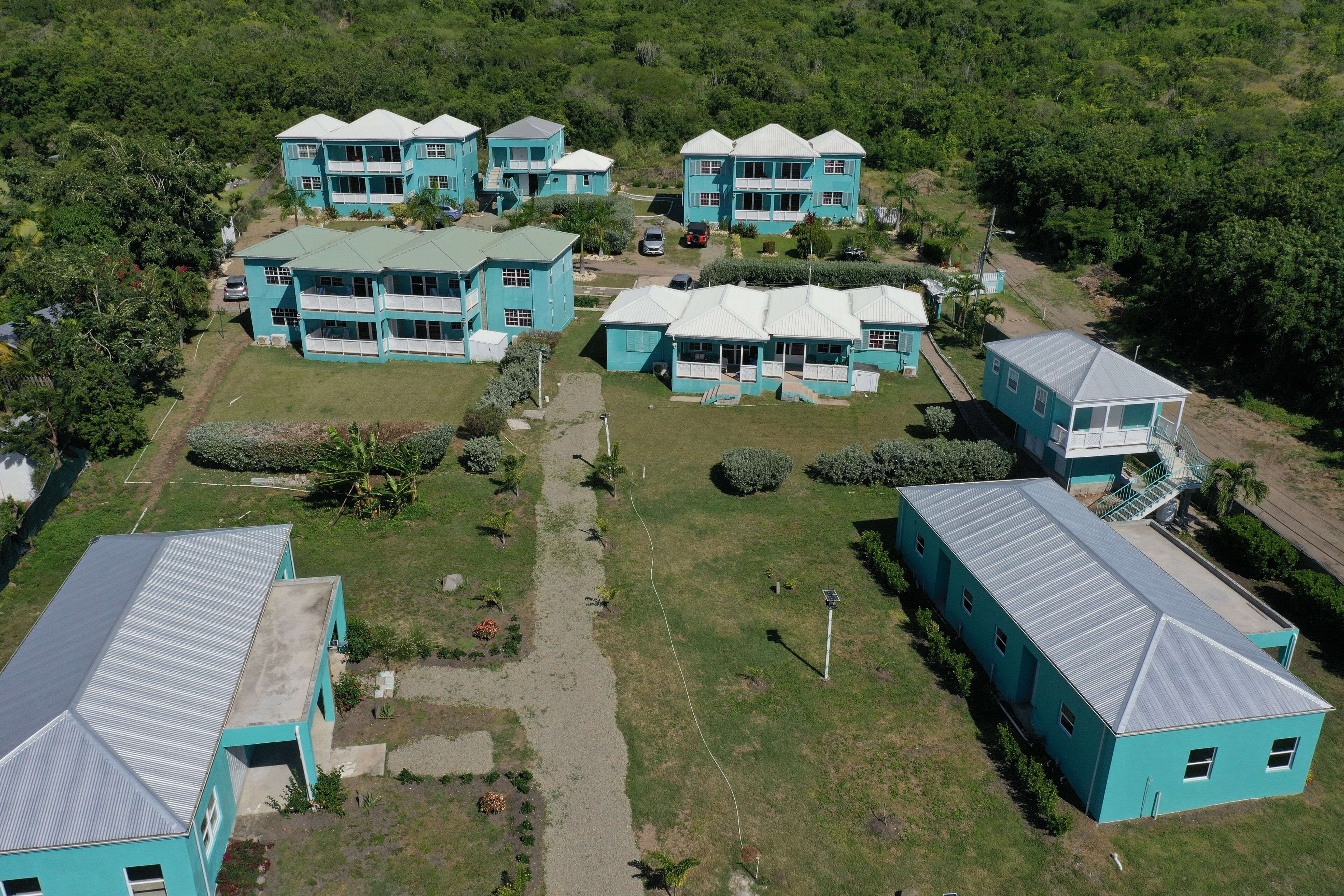 A cluster of turquoise buildings with multiple floors and balconies, surrounded by greenery and a clear sky.