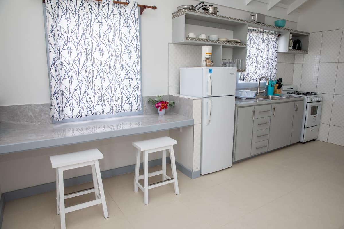 A kitchen with a white refrigerator, stove, and sink. There are two white stools and a vase with flowers on the counter.