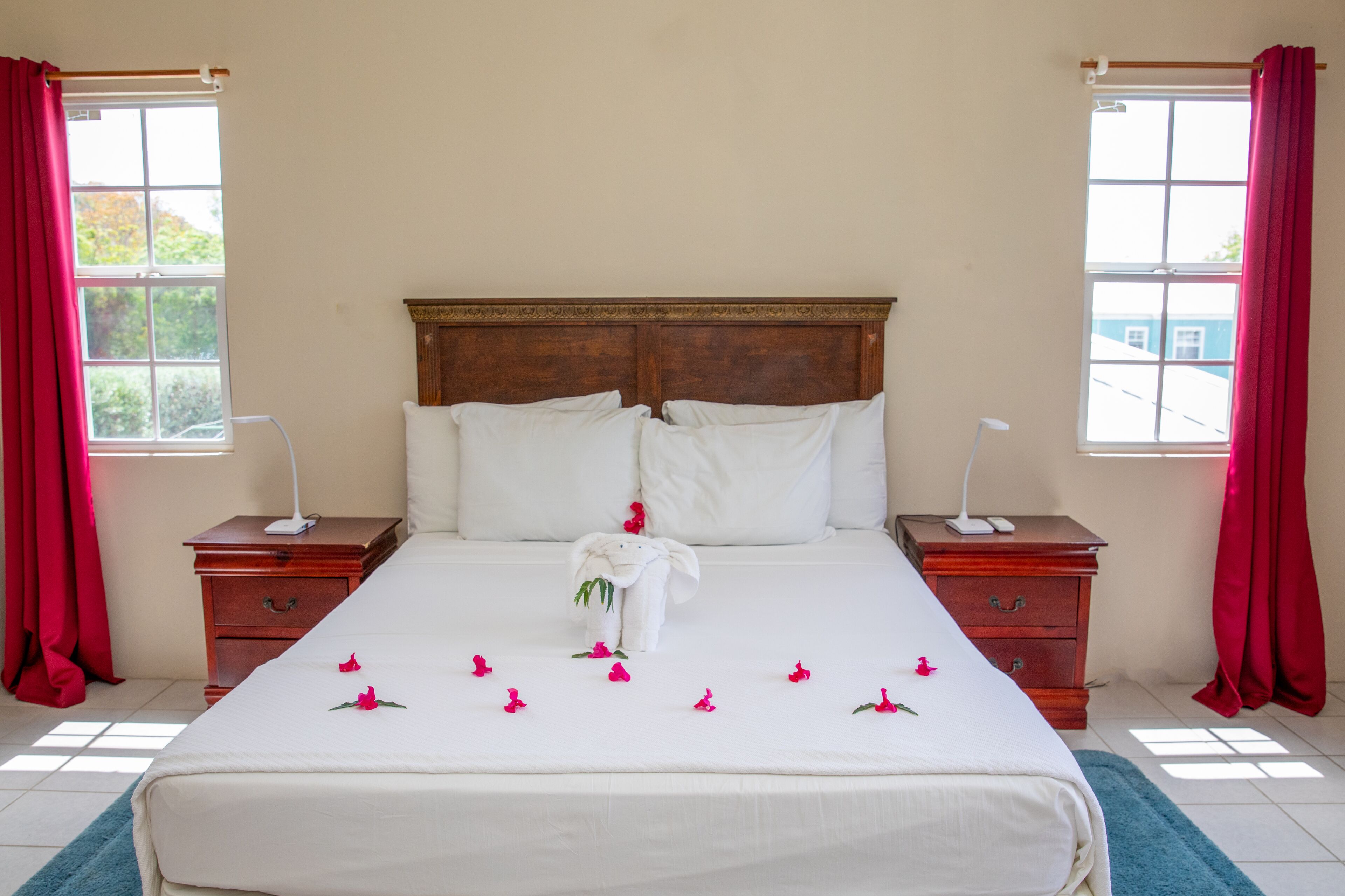 A hotel room with a large bed, two bedside tables, a wooden headboard, and red curtains.