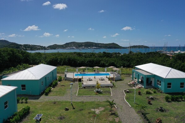 A property with two blue buildings, a swimming pool, and a view of the sea and hills. - Neem View Apartments Antigua (Falmouth Harbour)