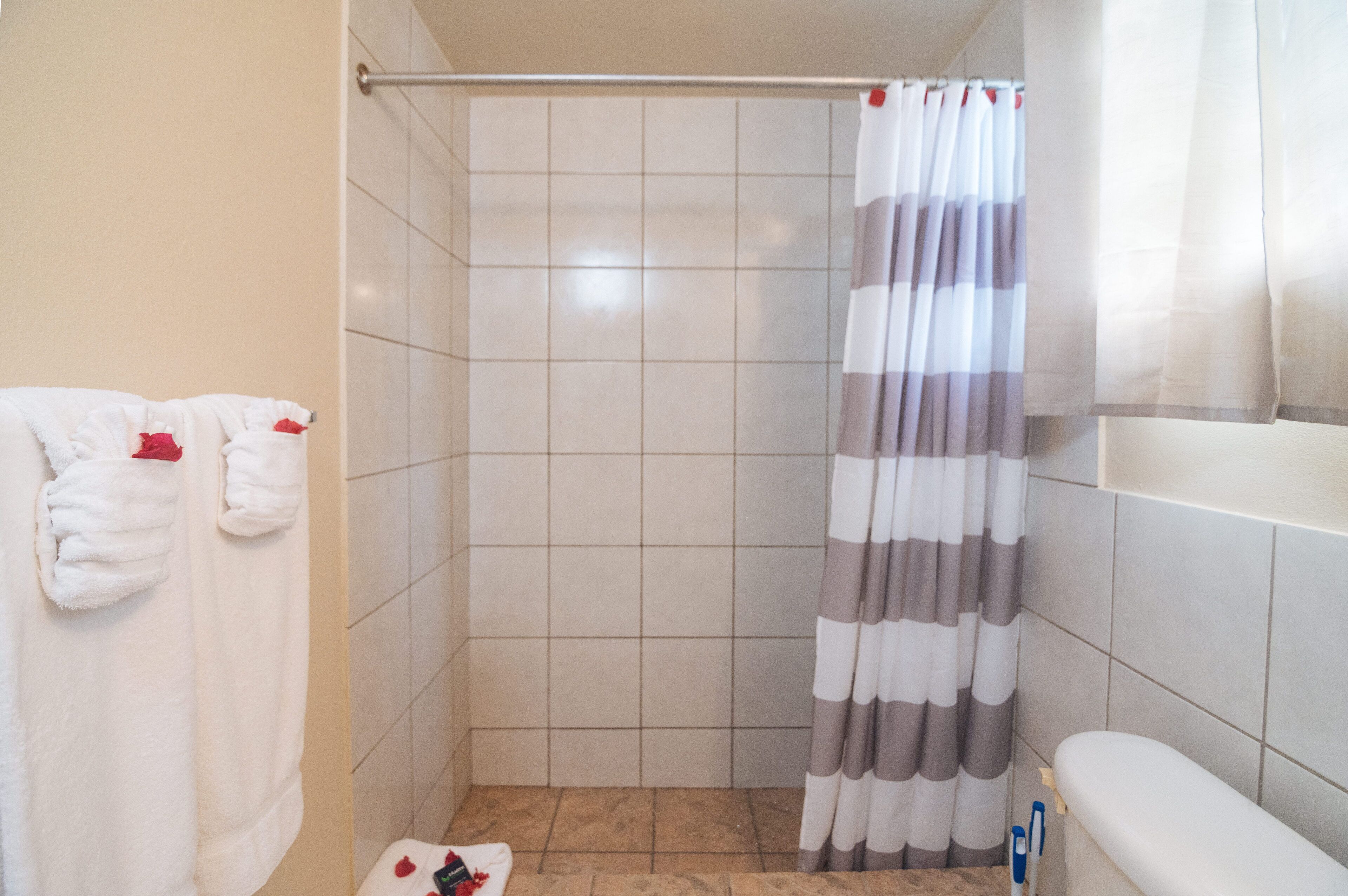 A small, tiled bathroom with a shower curtain, a toilet, and a towel rack with towels.
