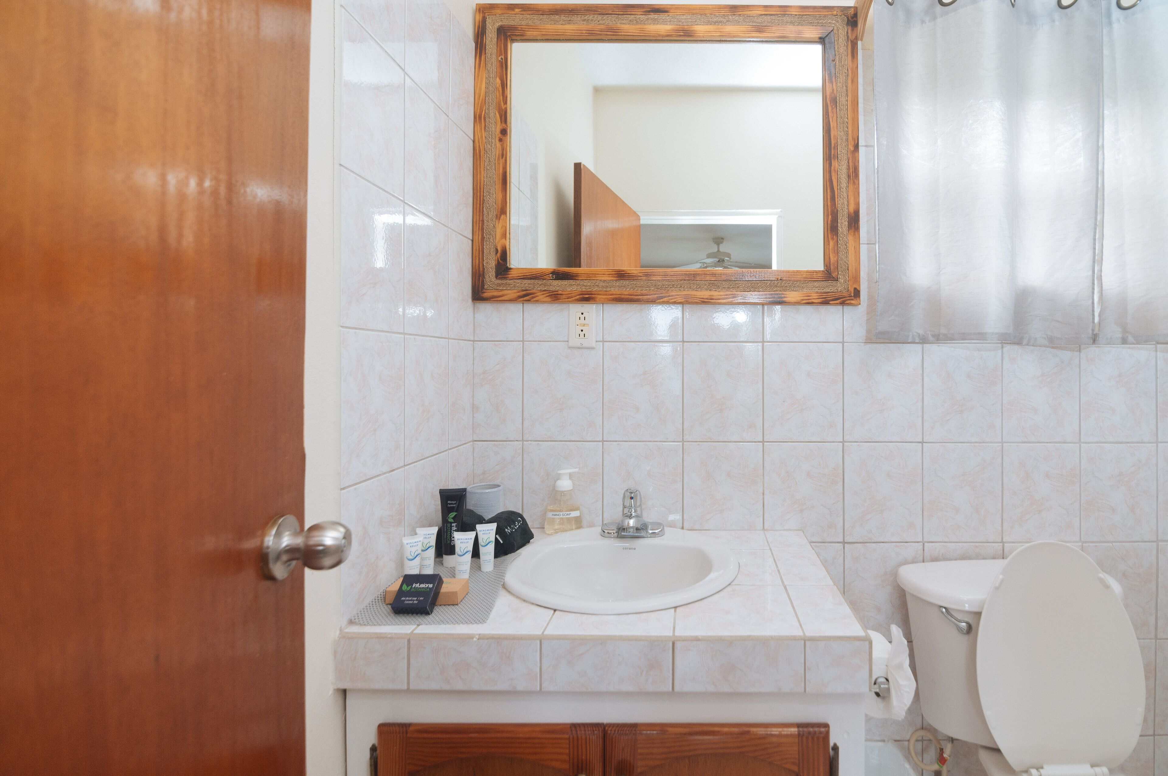 A bathroom with a wooden door, a white sink, a mirror, and a toilet.