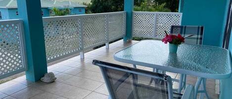A covered outdoor patio with a glass table and chairs, a white mesh chair, and a decorative vase with flowers.