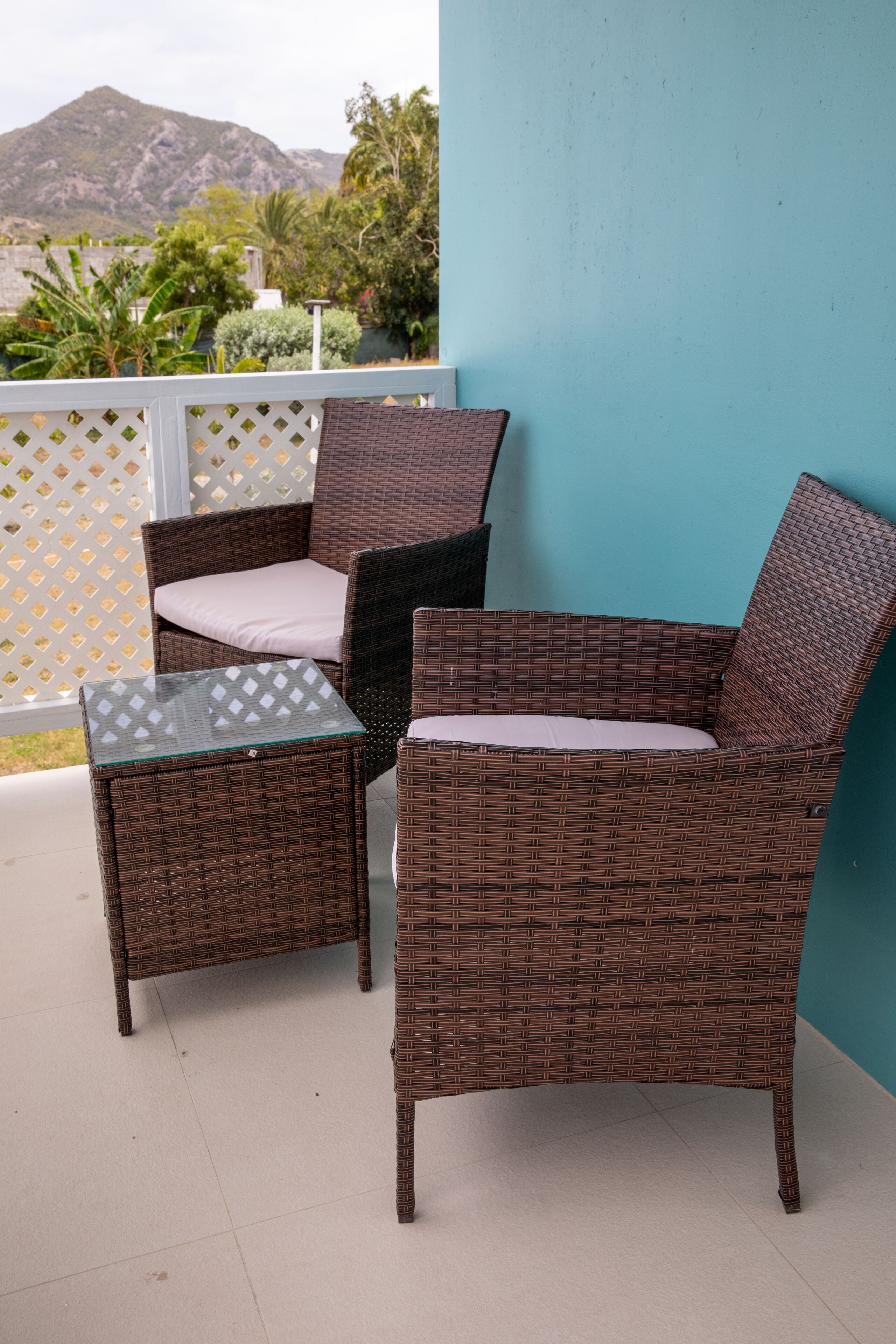 Un ensemble de chaise et de table en osier, placé devant un mur turquoise, avec une vue sur les montagnes et la verdure en arrière-plan.