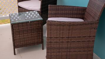 A wicker chair and table set against a turquoise wall, with a view of mountains and greenery in the background.