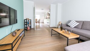 Un salon moderne avec un téléviseur à écran plat, une table basse en bois, un canapé gris et une bibliothèque.