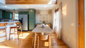 A modern kitchen with wooden flooring, a central island with bar stools, green cabinets, and a large refrigerator.
