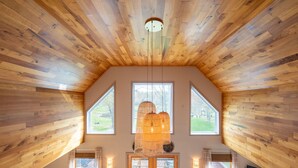 A spacious room with a sloped wooden ceiling, large windows, and a hanging light fixture.