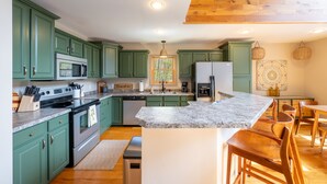 A kitchen with green cabinets, granite countertops, and wooden flooring.