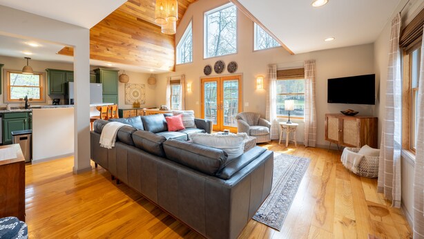 A spacious living area with a large gray sectional sofa, a wooden ceiling, and a kitchen in the background.