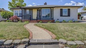 A single-story house with a front porch, a brick pathway leading to the door, and a small garden area.
