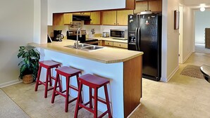 Une cuisine moderne dotée d’un îlot central, de meubles en bois, d’appareils électroménagers en acier inoxydable et de trois tabourets de bar rouges.