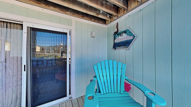 Une chaise Adirondack turquoise est posée sur une terrasse en bois, et une porte-fenêtre coulissante donne accès à un espace extérieur.
