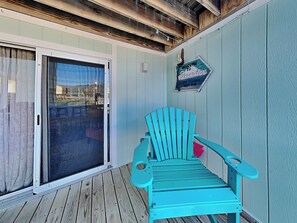 Une chaise Adirondack turquoise est posée sur une terrasse en bois, et une porte-fenêtre coulissante donne accès à un espace extérieur.