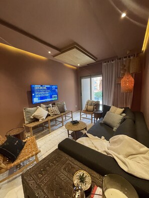 A modern living room with a large flat-screen TV, comfortable seating, and a large window. - Modern Two Bedroom Condo (Marrakech)