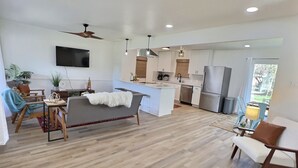 A modern living room with a grey sofa, wooden floor, and a flat-screen TV mounted on the wall. - Remodeled home with firepit! 1 mile to Randolph AFB & 3 parks! (Universal City)