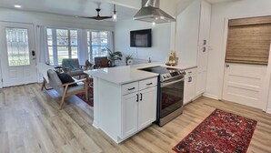 A modern kitchen with white cabinetry, a central island, stainless steel appliances, and a red patterned rug. - Remodeled home with firepit! 1 mile to Randolph AFB & 3 parks! (Universal City)