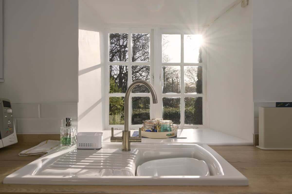 A modern kitchen with a sink, a window with a view of trees, and a white countertop.