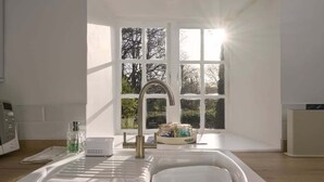 A modern kitchen with a sink, a window with a view of trees, and a white countertop. - Beautiful Thatched Cottage in Heart of Dartmoor (Newton Abbot)