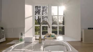 A modern kitchen with a sink, a window with a view of trees, and a white countertop.