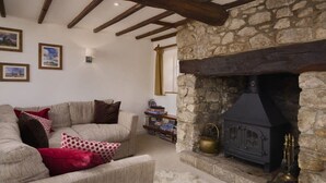 A cozy living room with a stone fireplace, wooden beams, and a sofa with patterned cushions. - Beautiful Thatched Cottage in Heart of Dartmoor (Newton Abbot)