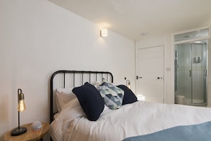 Een slaapkamer met een bed, kussens, een bedlampje, een ronde klok en een douchecabine van glas.