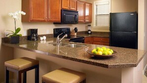 Una cocina con armarios de madera, un refrigerador negro, encimera de granito y un tazón de fruta.