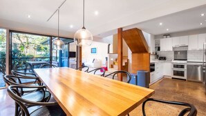 Une cuisine moderne avec des meubles blancs, des appareils en acier inoxydable et une table à manger en bois, accompagnée de chaises.