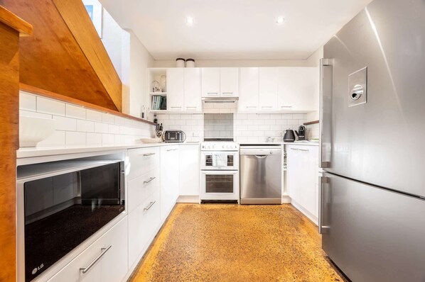 A modern kitchen with white cabinets, stainless steel appliances, and a speckled floor.