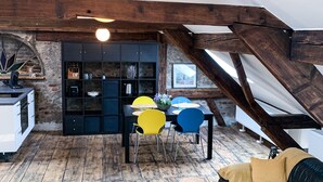 Un espace de vie de style loft avec des poutres en bois apparentes, un coin repas avec une table noire et des chaises jaunes, et un canapé noir avec des coussins jaunes.