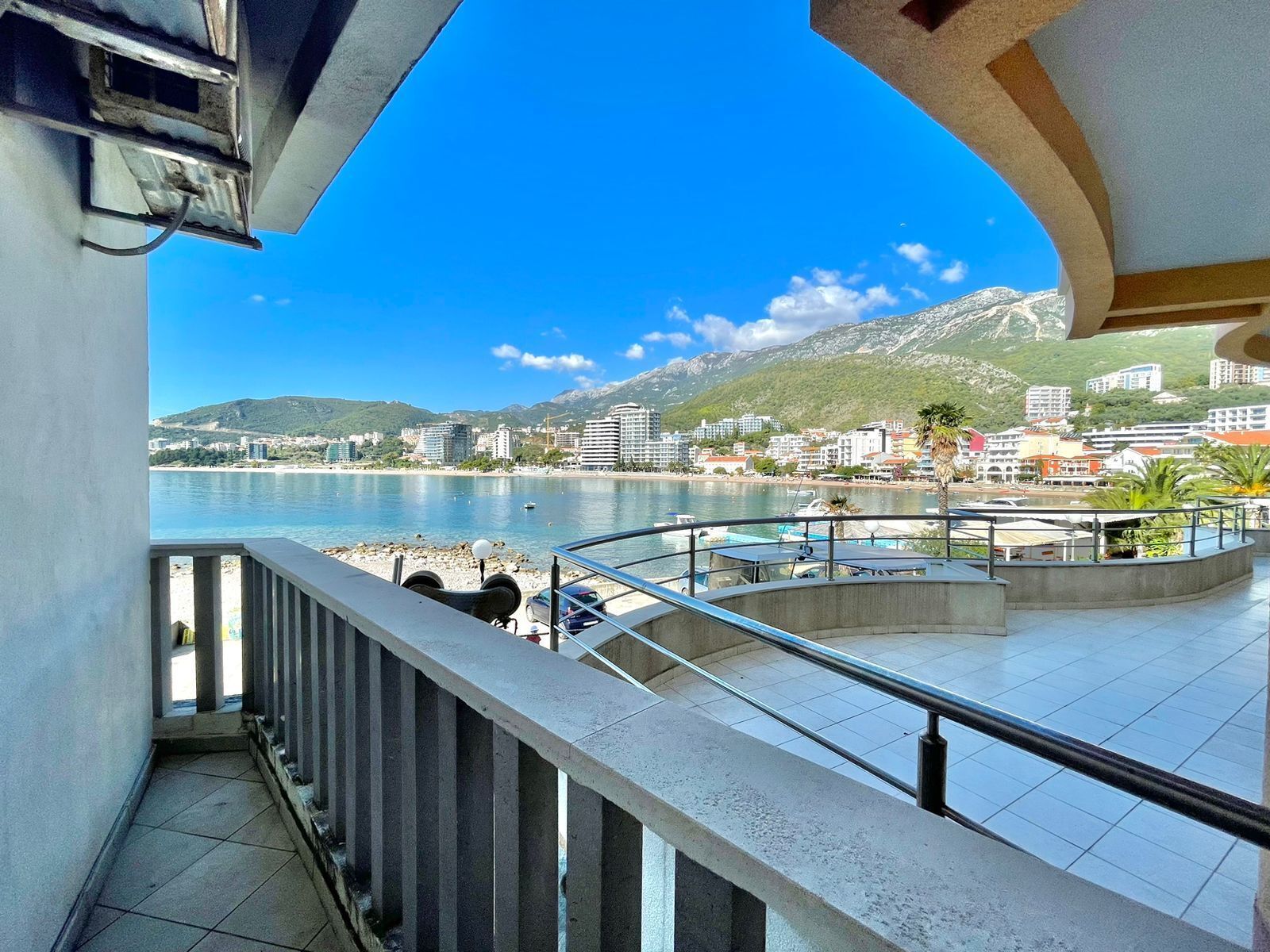 A balcony with a view of a coastal town, a body of water, and mountains in the background.