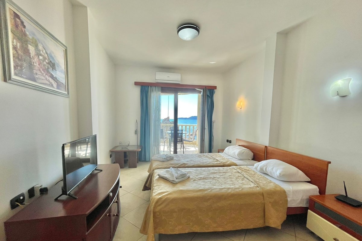 Une chambre d’hôtel avec deux lits, un bureau, une télévision et un balcon donnant sur la mer.