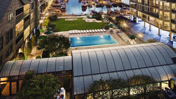 A hotel with a swimming pool, outdoor seating, and a view of a marina with boats.