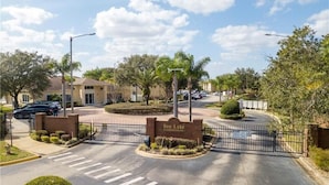 A gated entrance to Sun-Lake Condominium with a landscaped median, palm trees, and a clear sky. - Super close to Disney, 4BR/3BA,Next to the mall(restaurants) (Kissimmee)