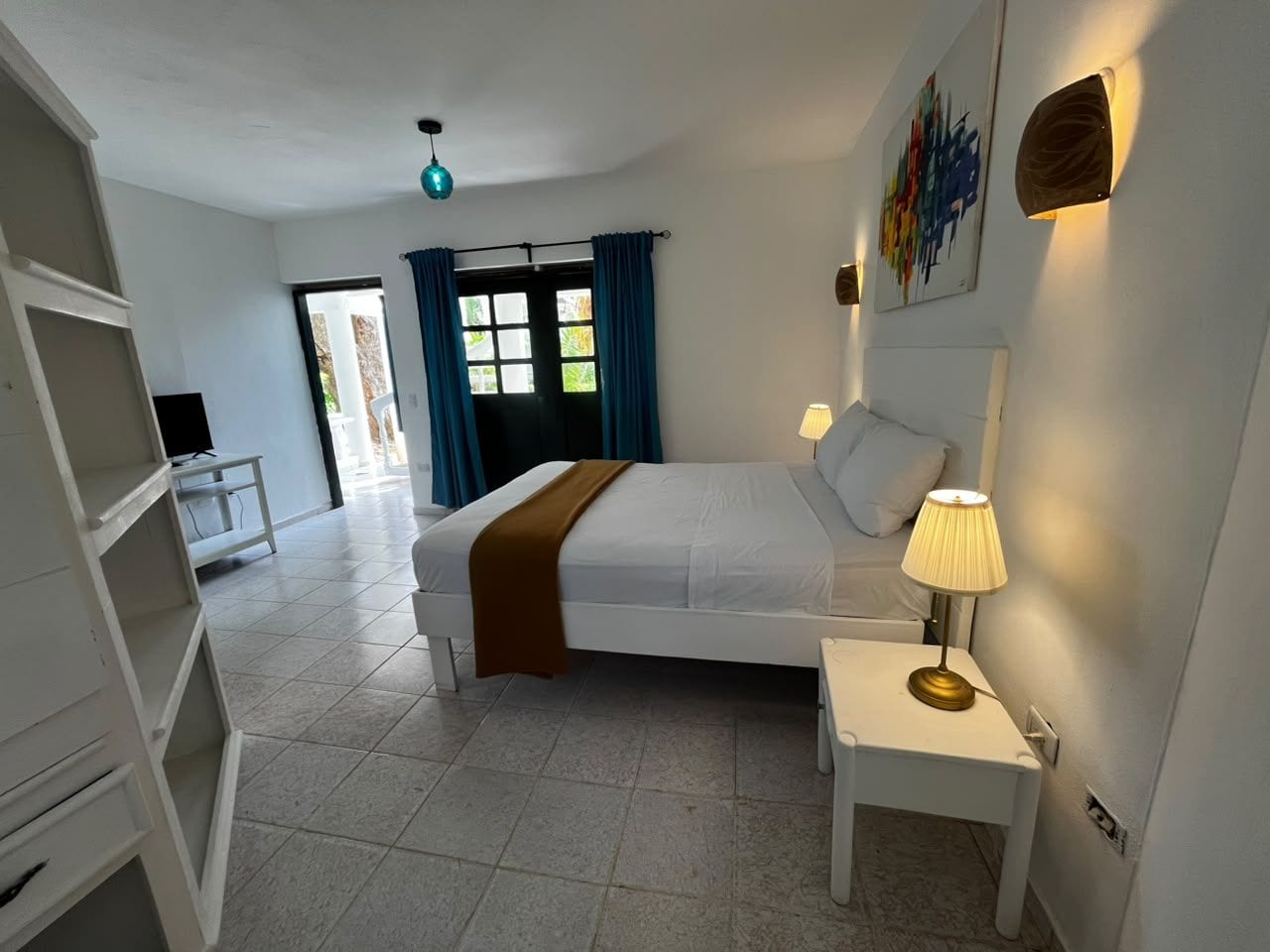 A bedroom with a bed, bedside lamp, and a view of the outside.
