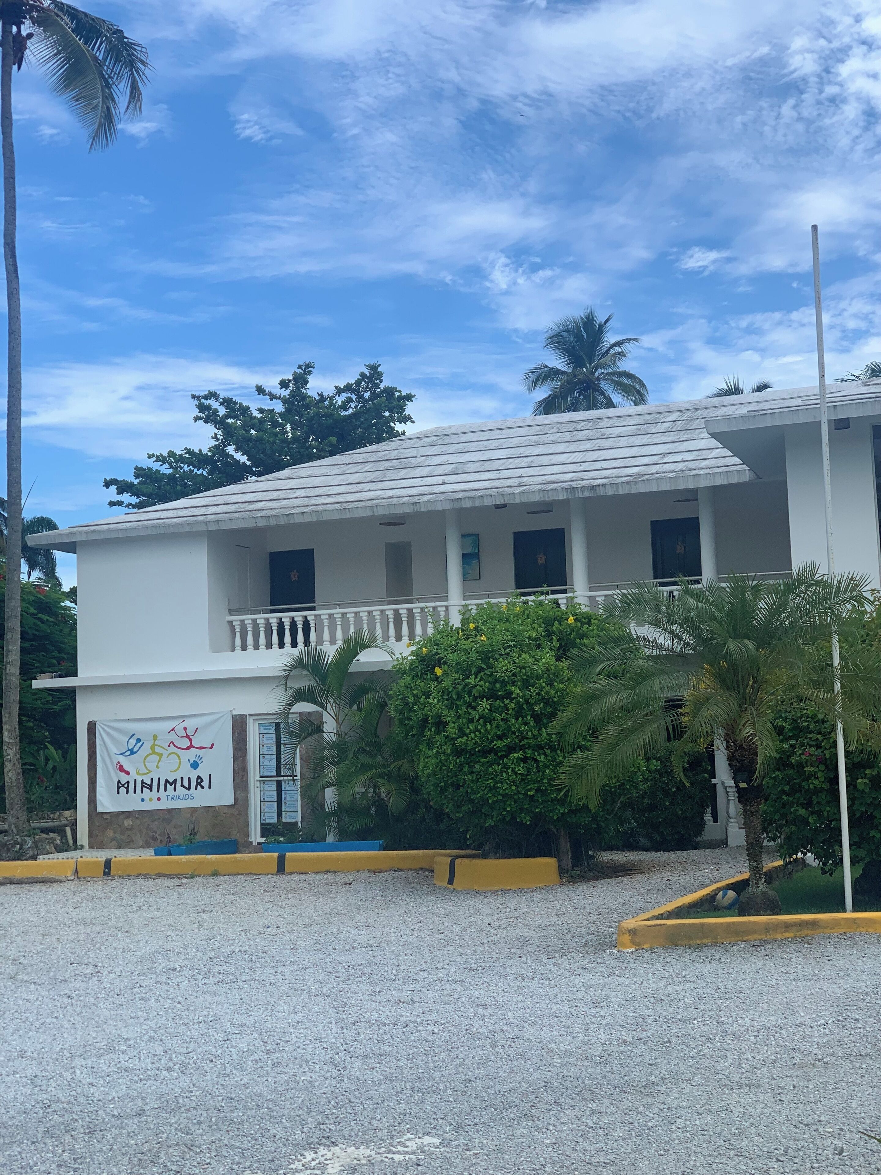 A two-story building with a white facade, a balcony on the upper floor, and a sign reading "MINIMURI TRIKIDS".